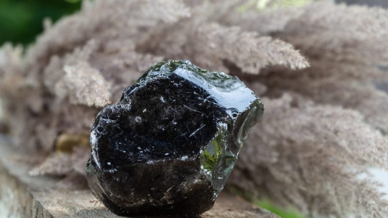 Black Obsidian Mineral Rock Sample over Wooden Background. Natural Volcanic Glass forms from Lava